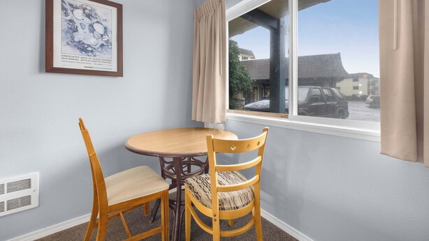 A room with a dining table and chairs, a framed artwork on the wall, and a window with curtains.