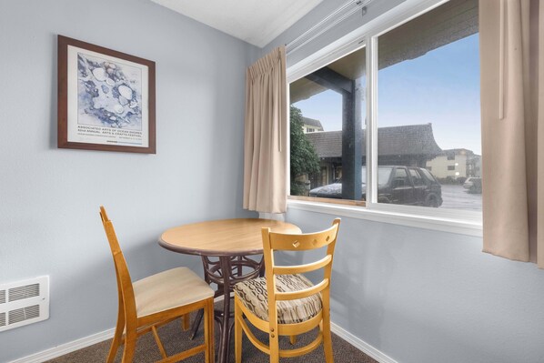 A room with a dining table and chairs, a framed artwork on the wall, and a window with curtains.
