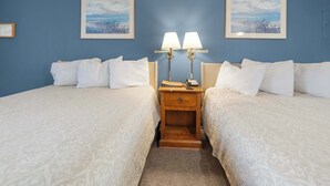 A hotel room with two beds, a wooden nightstand with lamps, and two framed pictures on the wall.