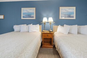 A hotel room with two beds, a wooden nightstand with lamps, and two framed pictures on the wall.