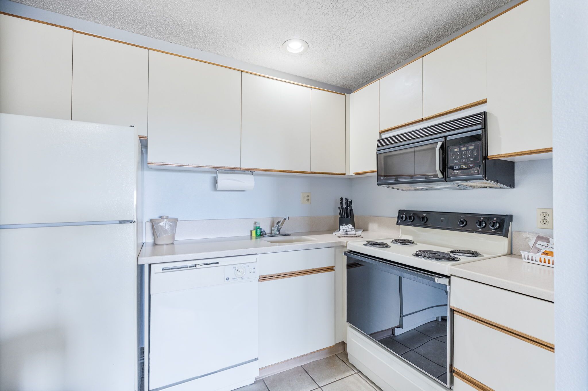 A compact kitchen with white cabinets, a built-in microwave, a stove, and a dishwasher.