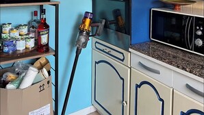 A kitchen with a microwave, oven, and a shelf with canned goods and a bottle.