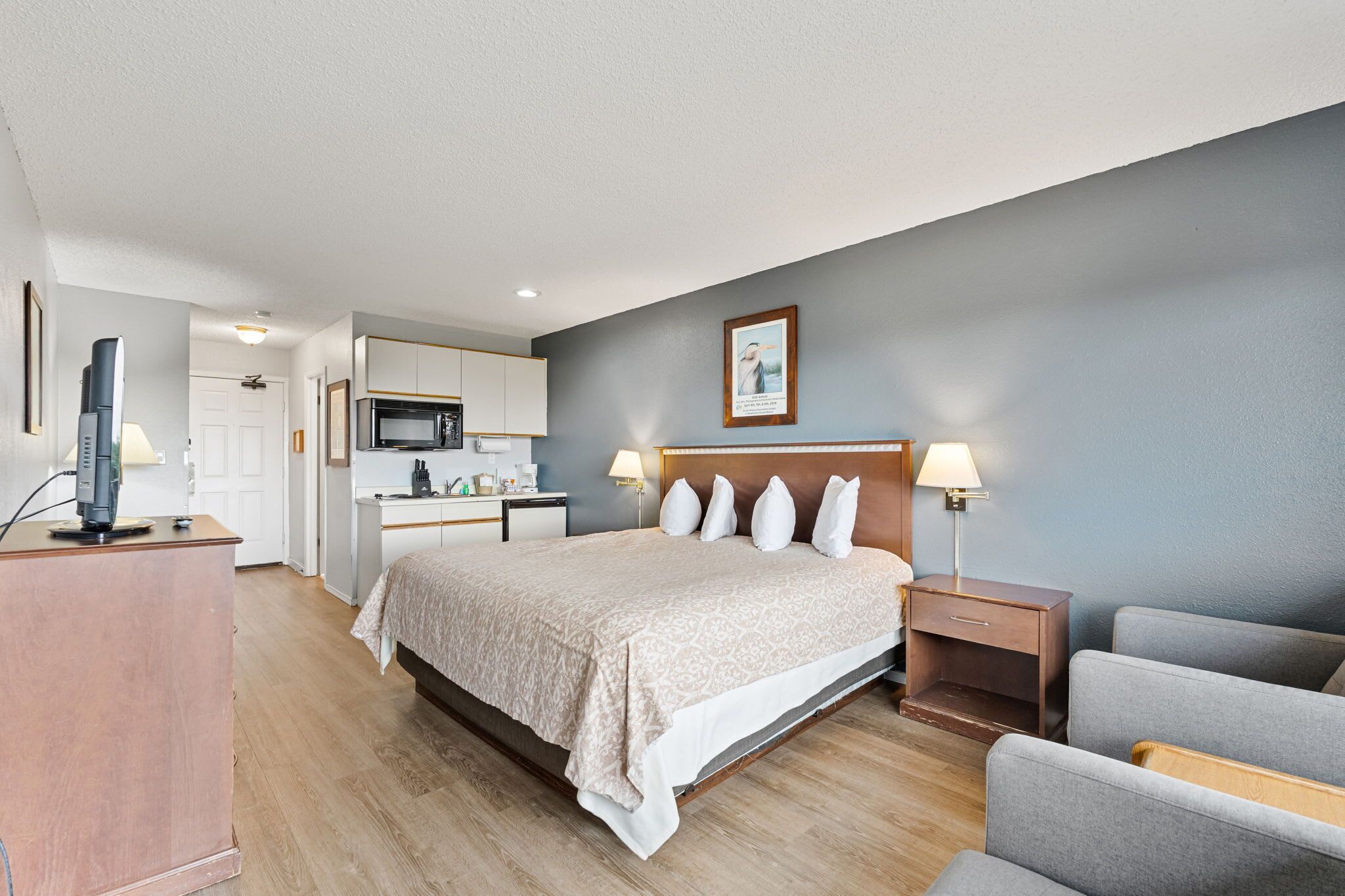 A hotel room with a bed, bedside tables, a desk, a chair, a television, and a kitchenette.