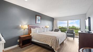 A hotel room with a bed, bedside lamps, a desk, a chair, a balcony with a view, and a television.