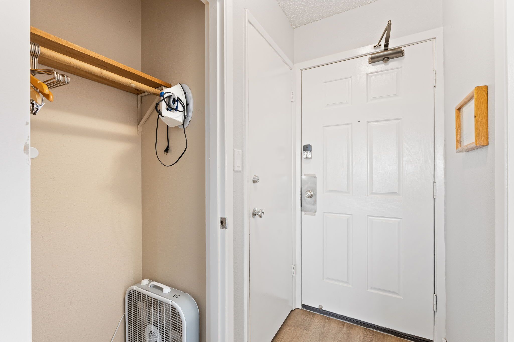 Una habitación con una puerta blanca, un equipo de aire acondicionado blanco y un estante de madera con un electrodoméstico blanco.