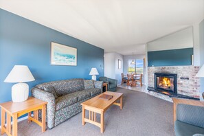 A living room with a sofa, two tables, a fireplace, and a painting on the wall. - 1-Bedroom Suite For 6 with Kitchen & Pool Access! (Ocean Shores)