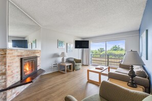 Una sala de estar con chimenea, televisor, sofá, mesa de centro y un balcón con vistas.