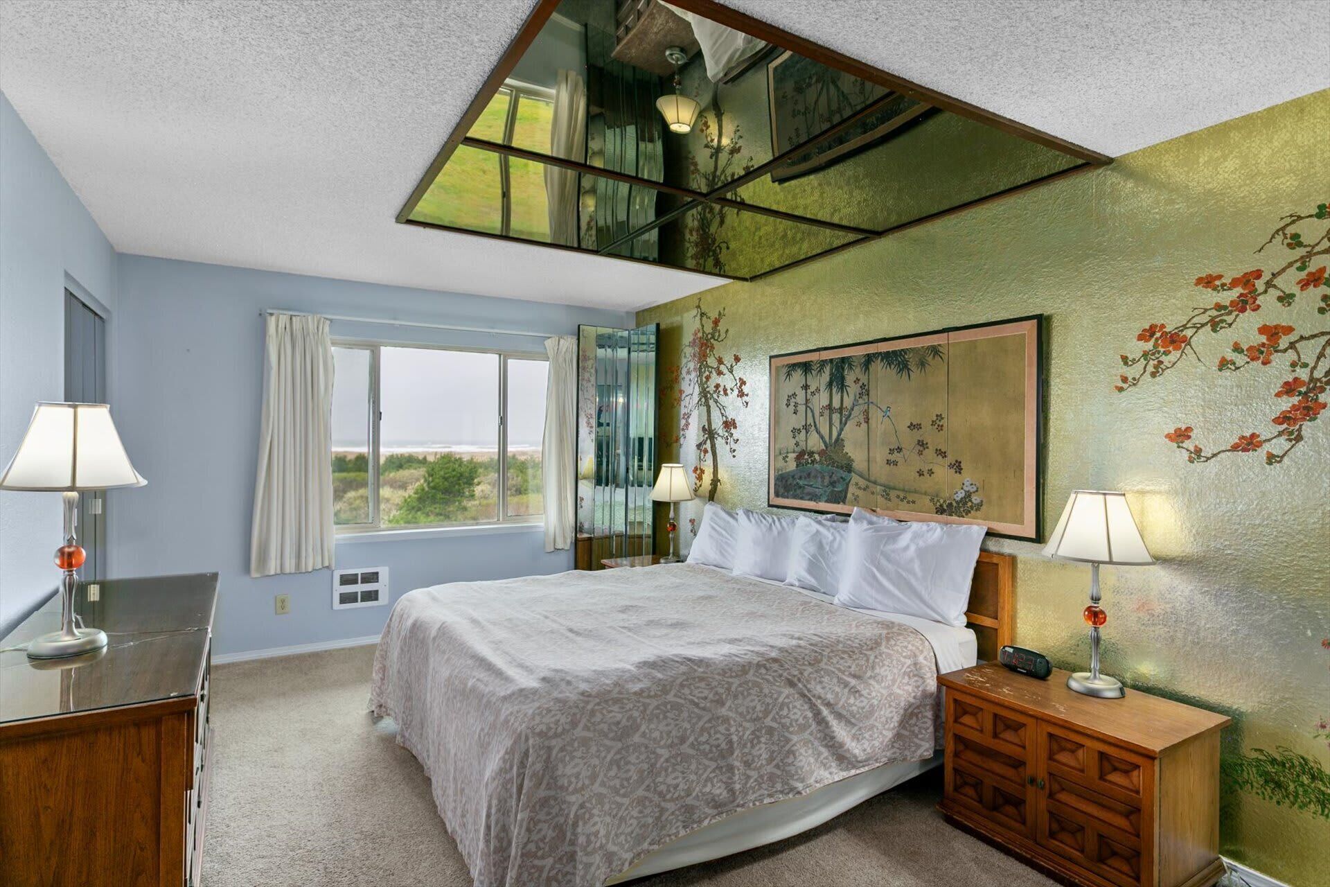 A bedroom with a bed, bedside tables, a window, and a painting on the wall.