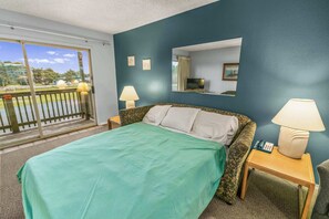 A hotel room with a bed, two bedside tables with lamps, a mirror, and a view of the outdoors. - 1-Bedroom Suite For 4 With King Bed & Pool Access (Ocean Shores)