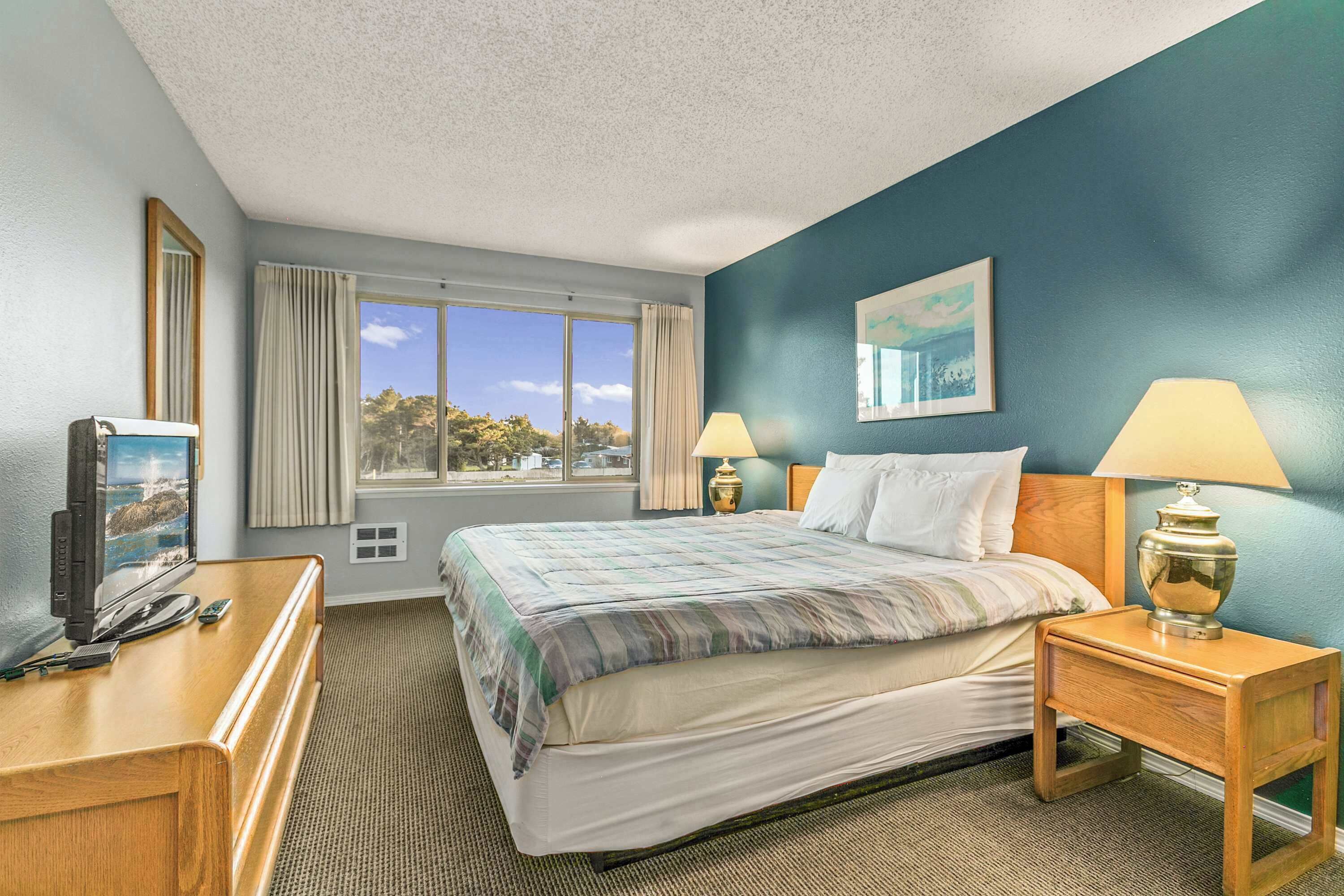 A hotel room with a bed, two bedside lamps, a television, and a window with curtains.
