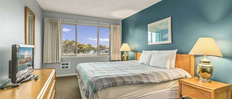 A hotel room with a bed, two bedside lamps, a television, and a window with curtains.