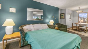 Quarto de hotel com uma cama, duas mesas de cabeceira com abajures, uma poltrona, uma escrivaninha com cadeiras e vista para o exterior.