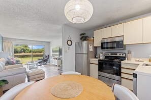 Eine moderne Küche mit Edelstahlgeräten, ein Essbereich mit Holztisch und Blick auf den Garten durch große Fenster.