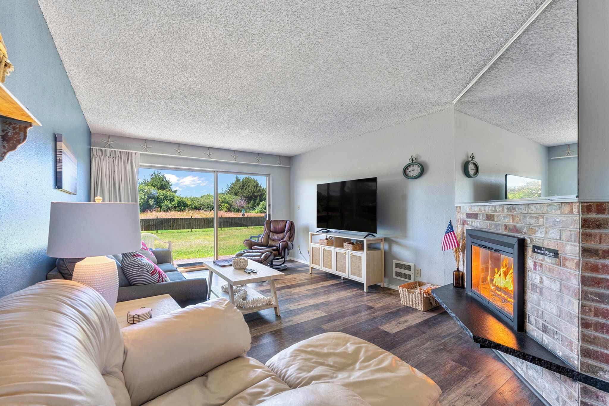 A living room with a fireplace, a television, and a large window overlooking a yard.