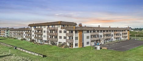 A multi-story hotel with balconies, a parking lot, and a grassy area.