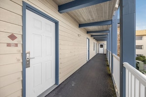 A corridor with doors, a metal handrail, and a covered walkway. - Pet-Friendly King Bed Studio with Pool & Hot Tub! (Ocean Shores)