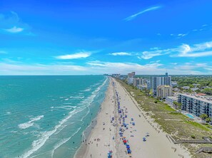 Eine Küstenstadt mit einem langen Strand, gesäumt von Gebäuden, darunter Hochhotels und Wohngebäude.