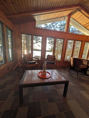 A wooden interior with large windows, a table with a decorative item, and seating with cushions.