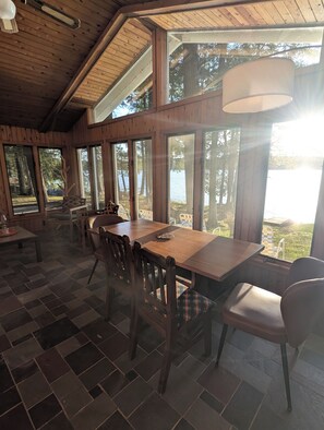 A wooden interior with large windows, a dining table, and chairs.
