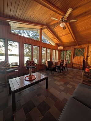 A wooden cabin interior with large windows, a dining table, and a ceiling fan.
