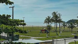 A coastal view with a playground, palm trees, and a beach in the background. - Pousada Cantinho do Mar (Bertioga)
