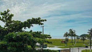 A view of a beach with palm trees, a playground, and a building in the foreground. - Pousada Cantinho do Mar (Bertioga)
