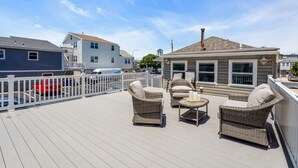 A deck with wicker furniture, a white fence, and a building in the background. - 4BR Beach Block Home w/ Washer-Dryer, Free Parking (Seaside Heights)