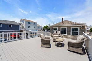 Eine Terrasse mit Korbmöbeln, einem weißen Zaun und einem Gebäude im Hintergrund.
