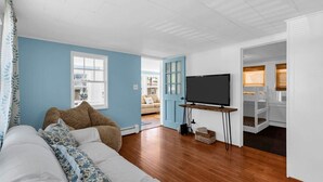 A room with a sofa, a television on a stand, a door leading to a balcony, and a view of the outside. - 4BR Beach Block Home w/ Washer-Dryer, Free Parking (Seaside Heights)