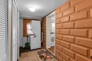 Ein schmaler Flur mit einem Kühlschrank, einem Mop und einem Teppich mit Blumenmuster.