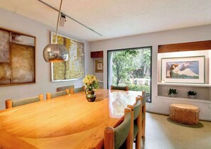 Uma sala de jantar com mesa de madeira, cadeiras, luminária pendente e obras de arte nas paredes.