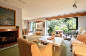 Ein Wohnzimmer mit Kamin, großen Fenstern und Blick auf Grünland.