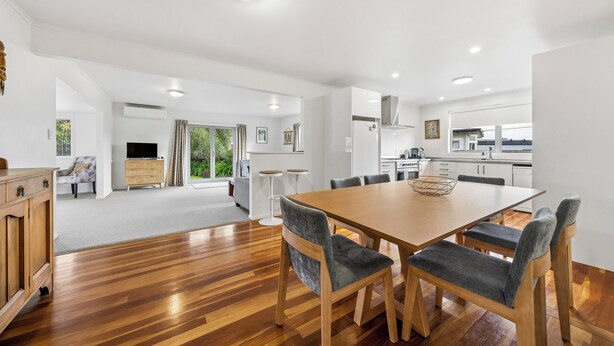 A spacious living area with a wooden dining table, grey upholstered chairs, and a view through a glass door to a garden. - Sundown on Cologne - Martinborough Holiday Home (Martinborough)