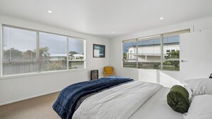 A bedroom with a bed, a chair, and large windows with blinds. - Sundown on Cologne - Martinborough Holiday Home (Martinborough)