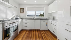 A modern kitchen with white cabinets, a stainless steel stove, and a window with a view. - Sundown on Cologne - Martinborough Holiday Home (Martinborough)