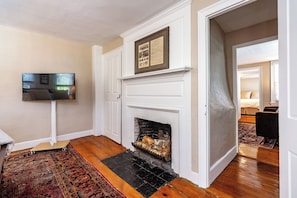A room with a fireplace, a television mounted on the wall, and a patterned rug on the floor. - Charming 3-bedroom apartment with AC in East Greenwich (East Greenwich)