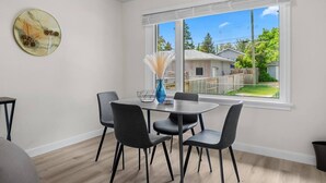 A dining area with a table and chairs, a vase with dried pampas grass, and a window with a view of a backyard. - 2 Bedroom + Pull out Sofa | Min to UofC (Calgary)