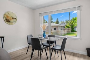 A dining area with a table and chairs, a vase with dried pampas grass, and a window with a view of a backyard. - 2 Bedroom + Pull out Sofa | Min to UofC (Calgary)
