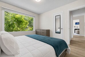 A bedroom with a bed, a dresser, a mirror, and a window with a view of greenery. - 2 Bedroom + Pull out Sofa | Min to UofC (Calgary)