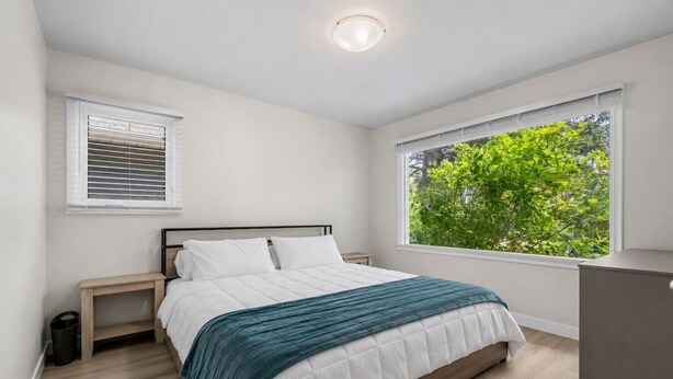A bedroom with a bed, a nightstand, a dresser, a window with a view of greenery, and a ceiling light. - 2 Bedroom + Pull out Sofa | Min to UofC (Calgary)
