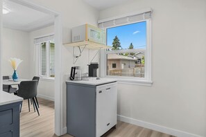 A compact kitchen with a built-in microwave, coffee maker, and dishwasher. A dining area with a table and chairs is visible through an open doorway. - 2 Bedroom + Pull out Sofa | Min to UofC (Calgary)