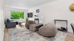 A modern living room with a sofa, two bean bags, a coffee table, and a TV mounted on the wall. - 2 Bedroom + Pull out Sofa | Min to UofC (Calgary)