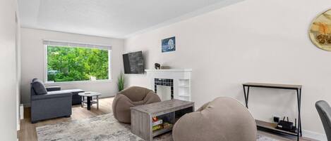 Un salon moderne avec un canapé, deux fauteuils poire, une table basse et un téléviseur fixé au mur.