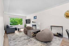 A modern living room with a sofa, two bean bags, a coffee table, and a TV mounted on the wall. - 2 Bedroom + Pull out Sofa | Min to UofC (Calgary)