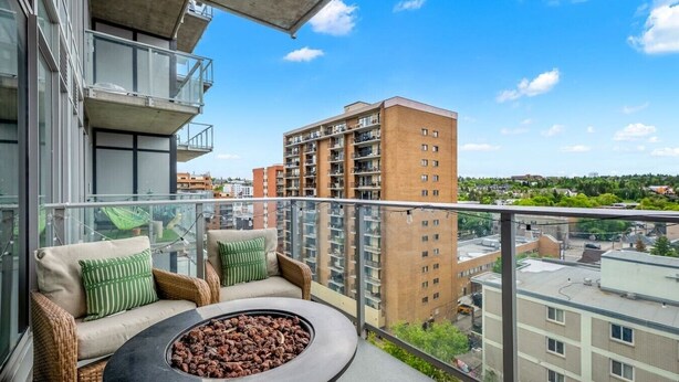 Een balkon met rieten meubilair, een vuurkorf en uitzicht op omliggende gebouwen.