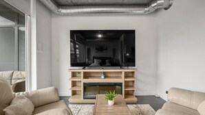 Een moderne woonkamer met een grote flatscreen televisie, houten wandplanken, een salontafel met een plant en beige leren banken.