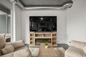 A modern living room with a large flat-screen TV, wooden shelving, a coffee table with a plant, and beige leather sofas. - `The Cedar` | Mins to Stampede | Patio Fire-pit (Calgary)