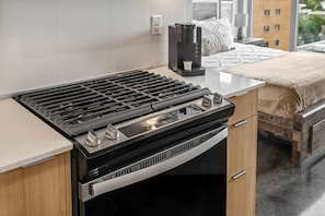 A kitchen with a gas stove, coffee maker, and a bed with a view. - `The Cedar` | Mins to Stampede | Patio Fire-pit (Calgary)