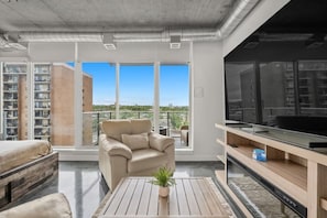A modern apartment with a large window, a sofa, a TV, and a dining area. - `The Cedar` | Mins to Stampede | Patio Fire-pit (Calgary)