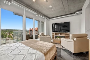 A modern hotel room with a large bed, two sofas, a TV, and a balcony with a city view. - `The Cedar` | Mins to Stampede | Patio Fire-pit (Calgary)